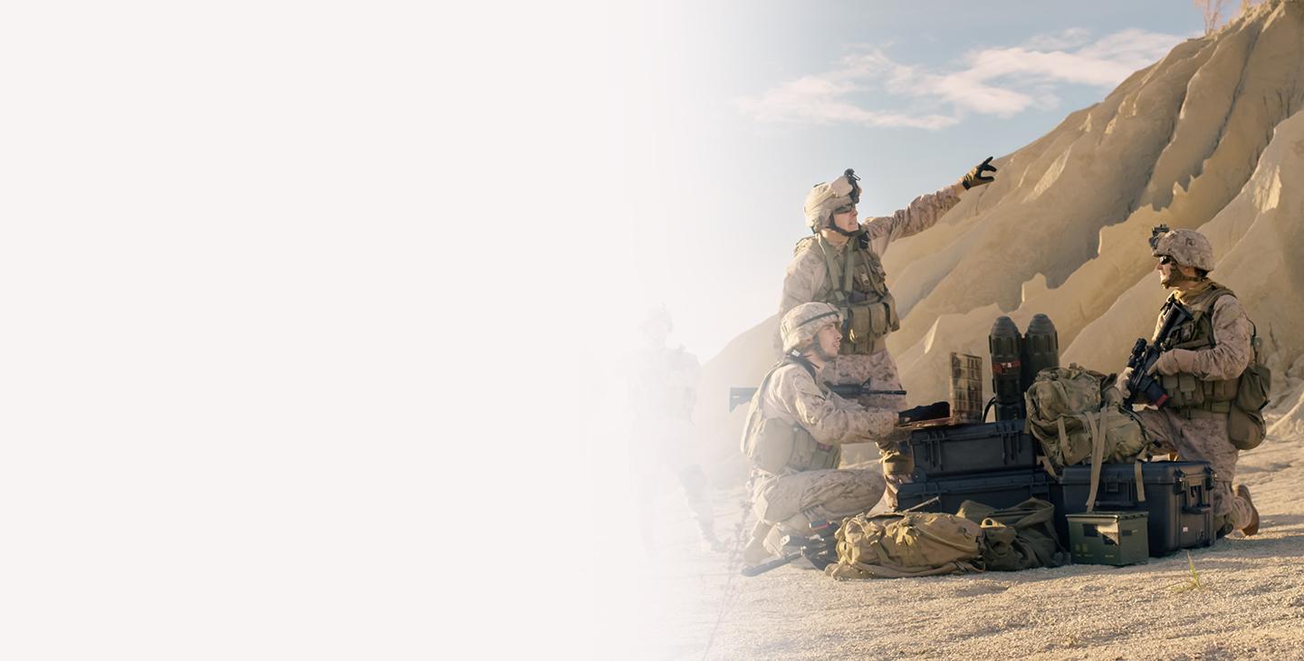 三名身穿战斗装备的士兵在沙丘脚下的战斗装备旁交谈